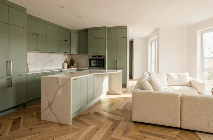 Cuisine ouverte rénovée avec armoires vert sauge, îlot en porcelaine et parquet en chêne en chevron