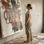 Jeune artiste contemporaine examinant une grande toile abstraite dans son atelier urbain aux murs en béton brut